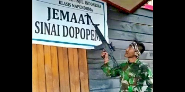 Foto salah satu anggota TNI membawa senjata laras panjang dan mengangkatnya di depan papan nama sebuah gereja/Net